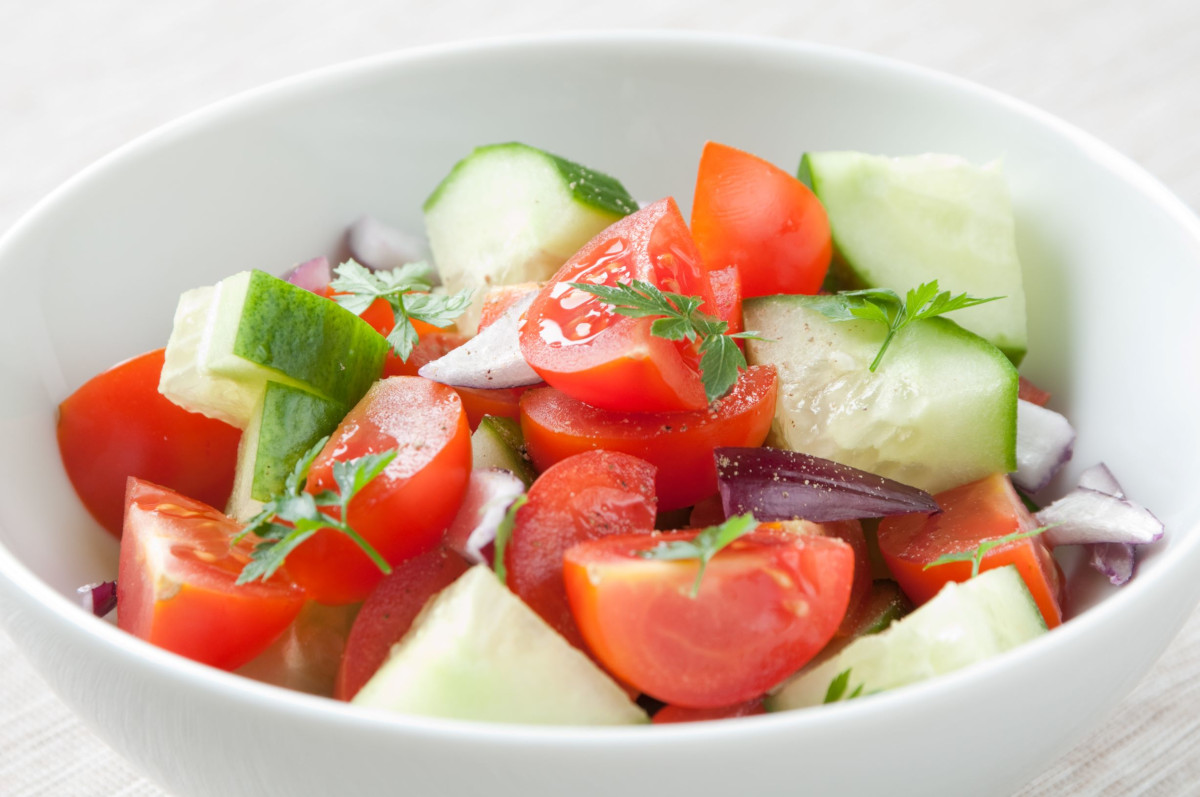 A bowl of salad with tomato, cucumber, red onion and fresh herbs