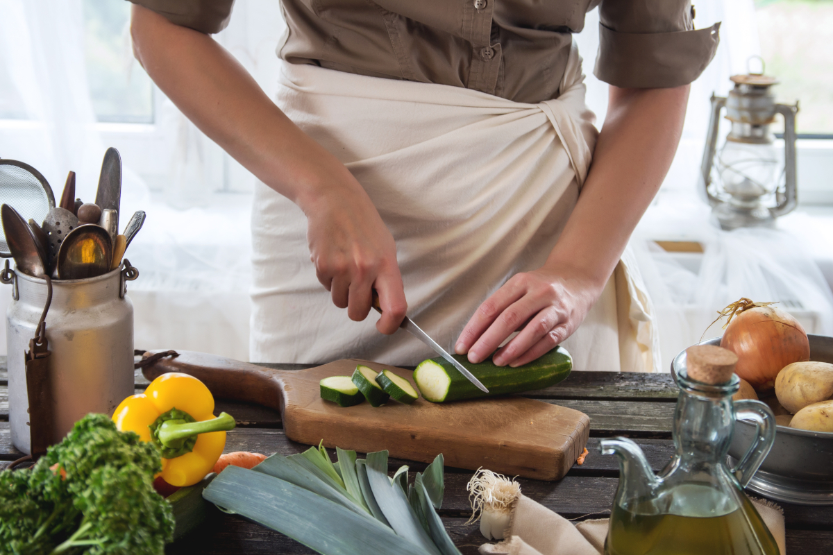 A woman slices a zucchini squash on a cutting board
