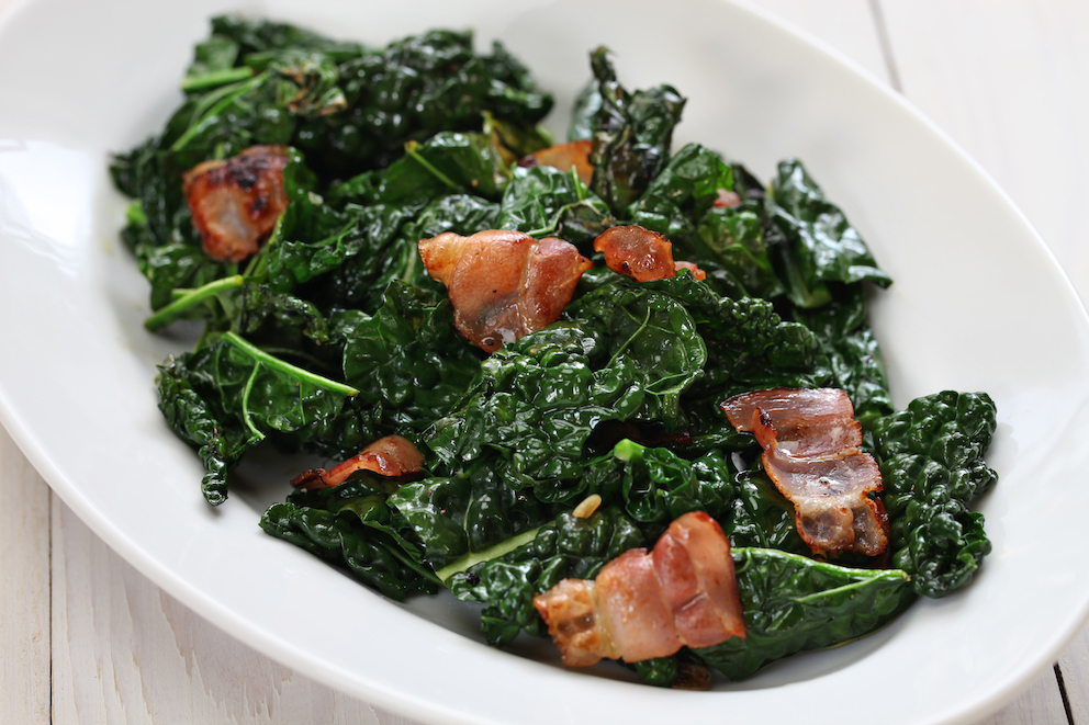 A bowl of cooked kale with pieces of bacon
