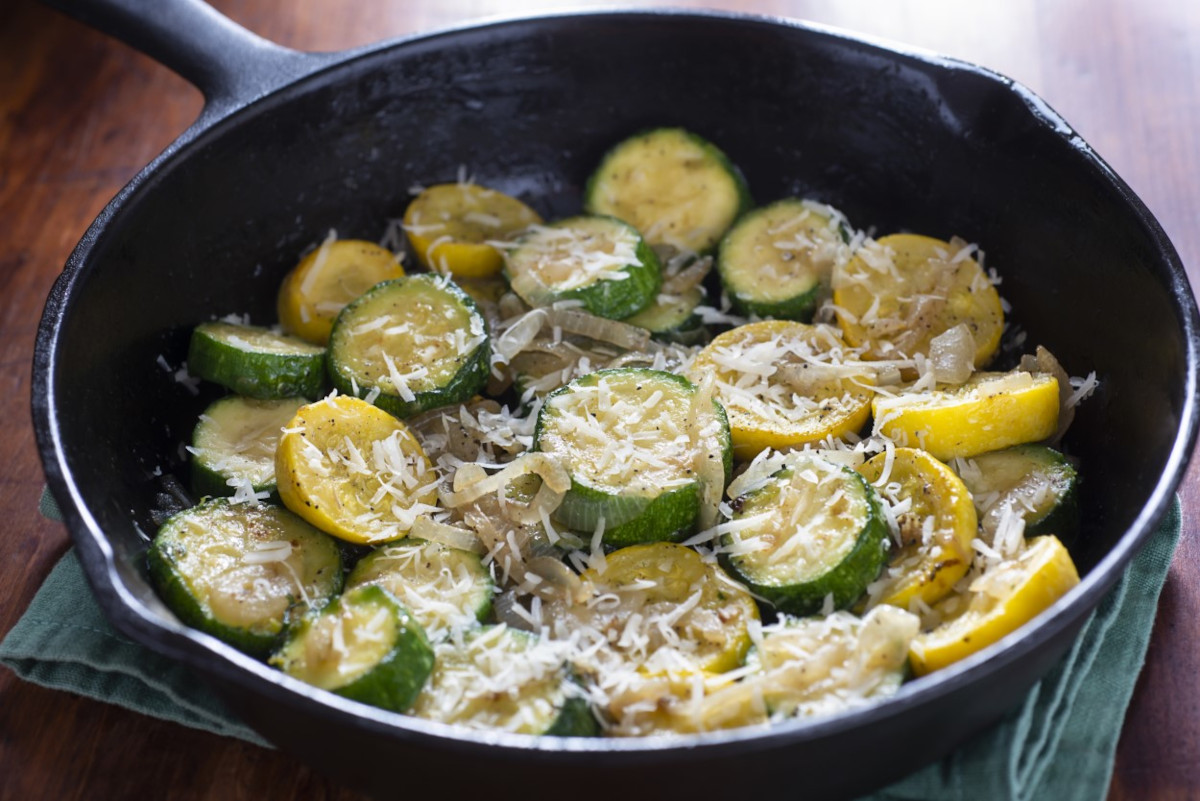 A skillet with zucchini and summer squash topped with grated cheese