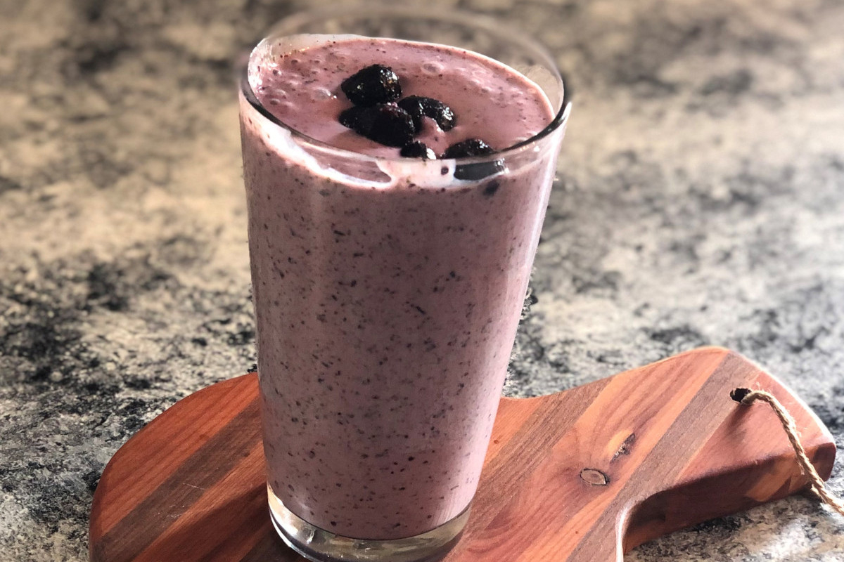 A glass of blueberry spinach smoothie topped with blueberries