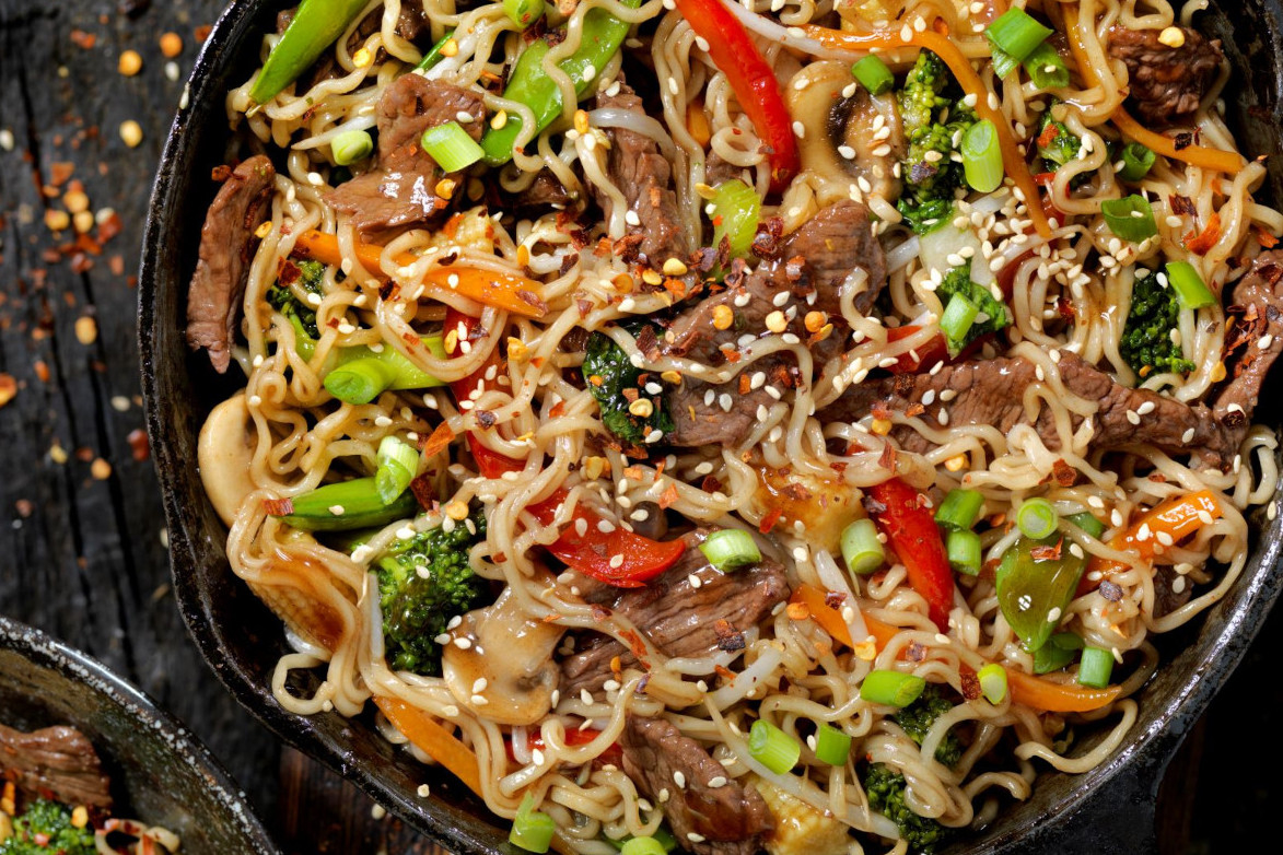 A skillet with noodles, red bell pepper, broccoli, beef and sesame seeds