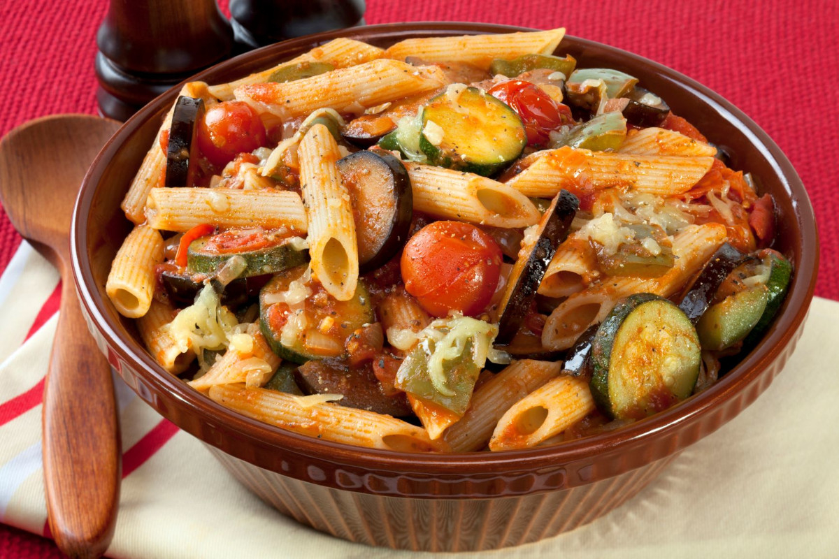A bowl of penne noodles with baked cherry tomatoes and zucchini