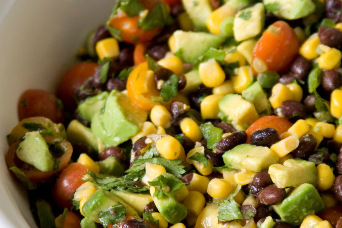 A bowl with corn, black beans, avocado, tomatoes and cilantro