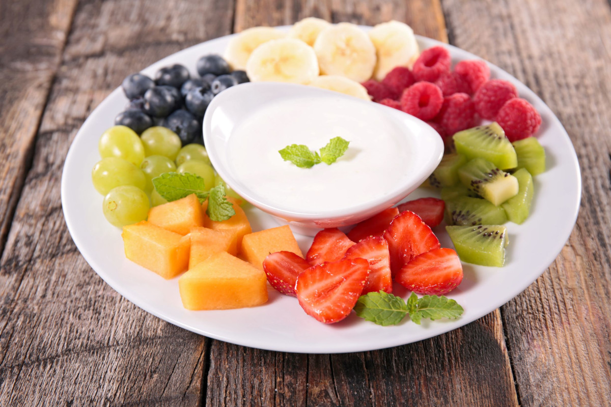 A platter with different fruit with fruit dip in the center
