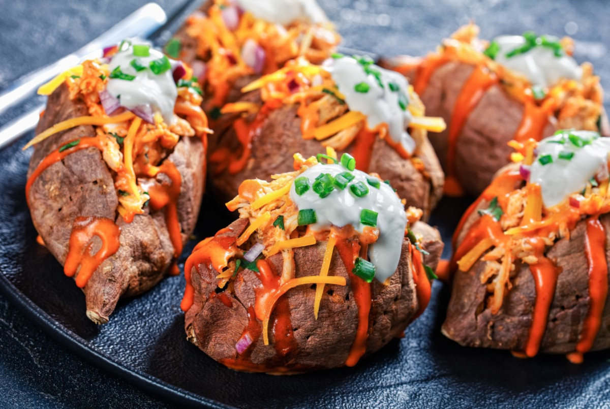 A plate of baked potatoes topped with dressing, sour cream and herbs