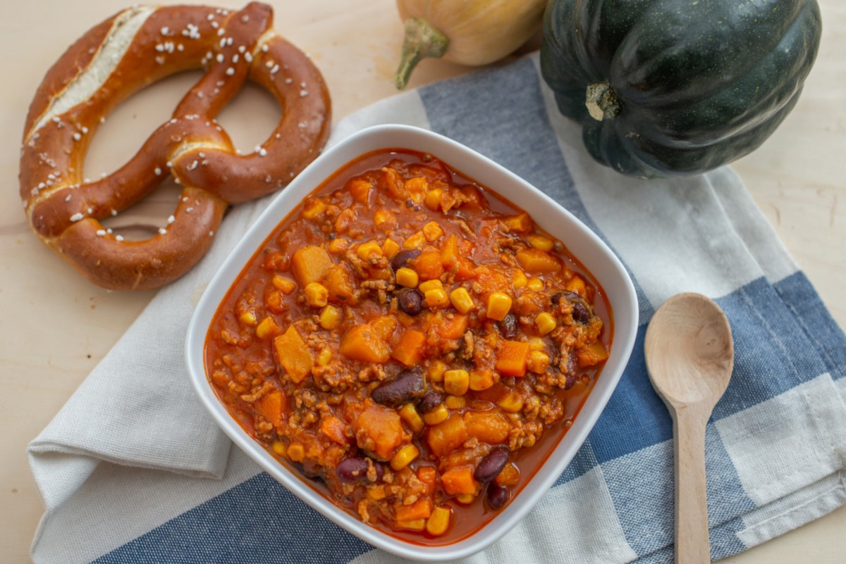 A bowl of pumpkin chili with a soft pretzel