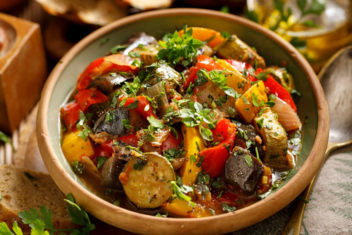 A bowl of ratatouille with colorful vegetables topped with herbs