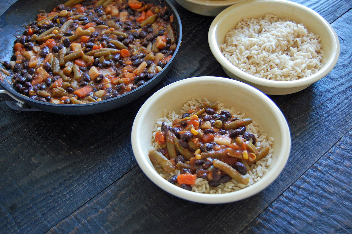 A serving bowl of beans and vegetables and two bowls with rice