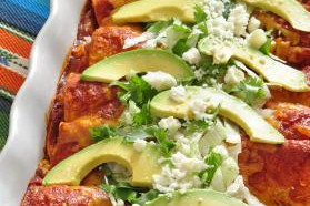 A casserole dish with enchiladas topped with avocado slices, cheese and cilantro
