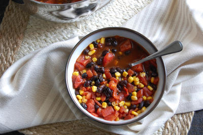 A bowl of soup with black beans, tomato and corn