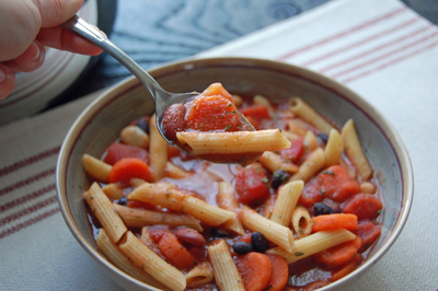 A bowl of penne noodles with vegetables and tomato broth