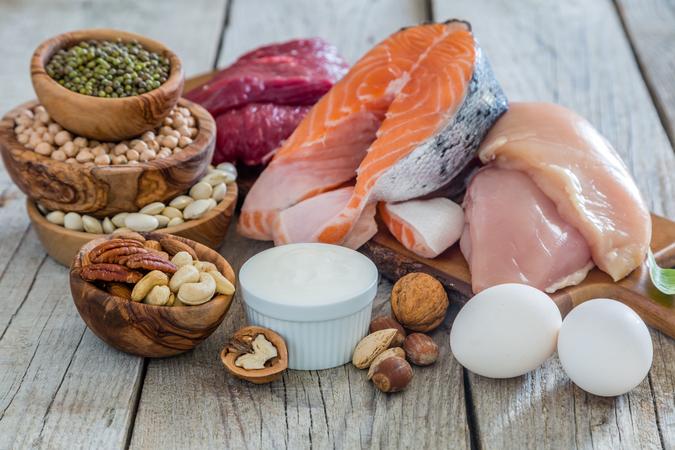 Various protein foods including raw salmon, chicken, beef, eggs, nuts and seeds