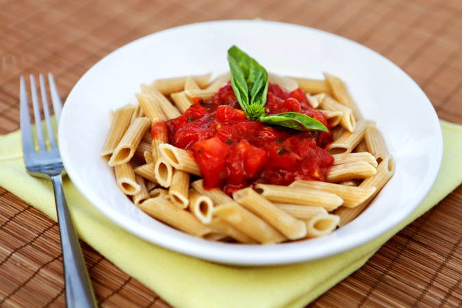 A bowl of penne noodles with marinara sauce and fresh basil