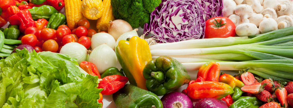 An assortment of fresh vegetables including lettuce, onions, red cabbage, bell peppers, tomatoes, mushrooms, corn and scallions